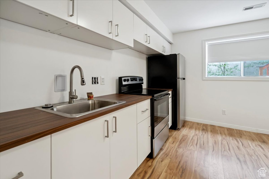 Kitchen with appliances with stainless steel finishes, a sink, light wood finished floors, and white cabinetry
