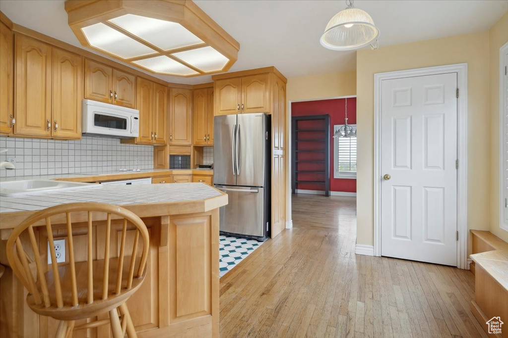Kitchen with freestanding refrigerator, white microwave, tile counters, light wood finished floors, and tasteful backsplash