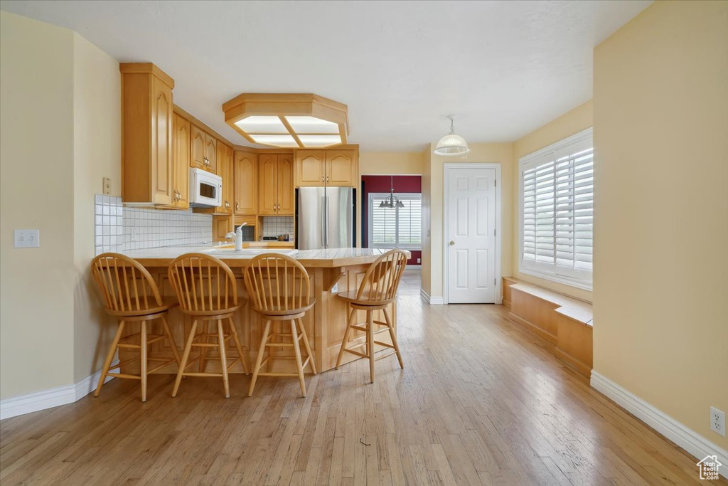 Kitchen featuring white microwave, freestanding refrigerator, light countertops, light wood-style flooring, and baseboards
