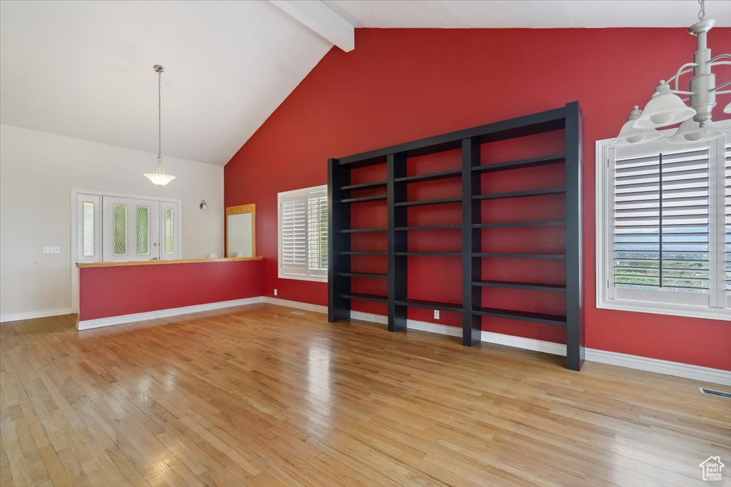Empty room with light wood finished floors, healthy amount of natural light, beam ceiling, baseboards, and high vaulted ceiling