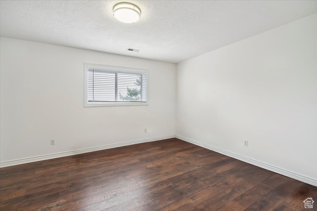 Empty room with dark wood-style flooring, baseboards, and a textured ceiling