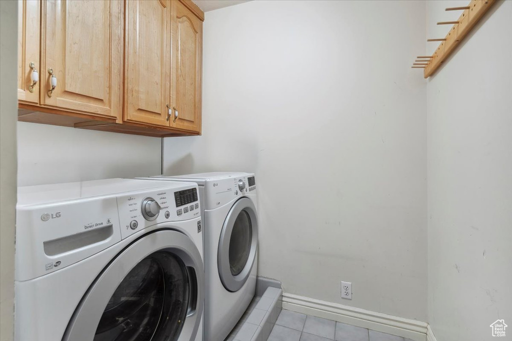 Washroom featuring independent washer and dryer, light tile patterned floors, cabinet space, and baseboards