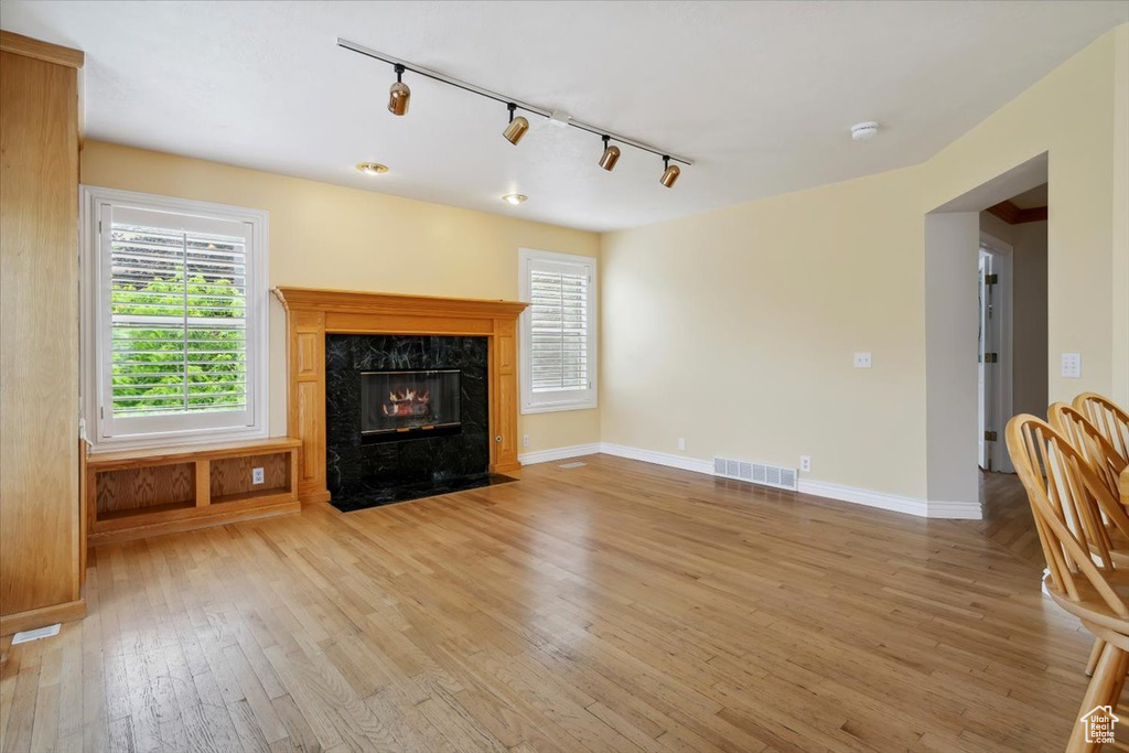 Unfurnished living room featuring track lighting, light wood finished floors, plenty of natural light, and a high end fireplace