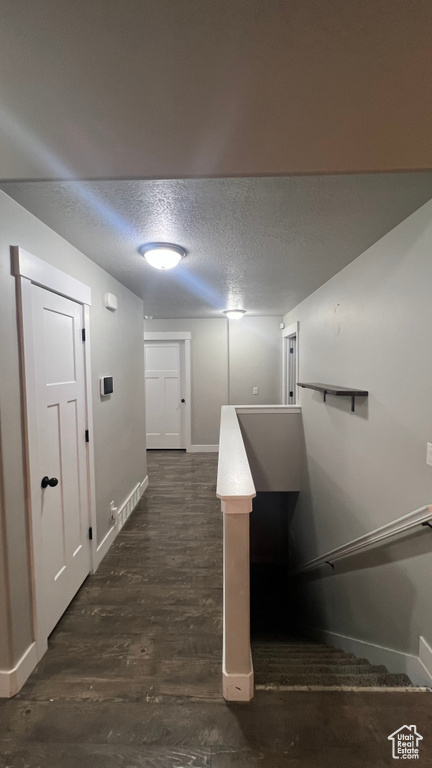 Hall with a textured ceiling and dark wood-style flooring
