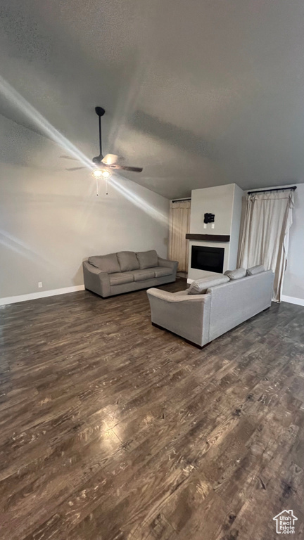 Living area with dark wood finished floors, ceiling fan, a fireplace, and a textured ceiling