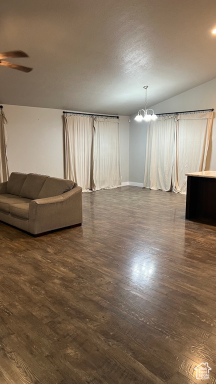 Unfurnished living room with a chandelier, a ceiling fan, dark wood-style floors, and lofted ceiling