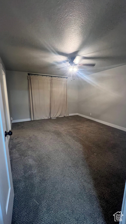 Unfurnished bedroom featuring a textured ceiling, dark carpet, and a ceiling fan