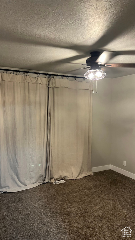 Empty room with dark colored carpet, a ceiling fan, and a textured ceiling