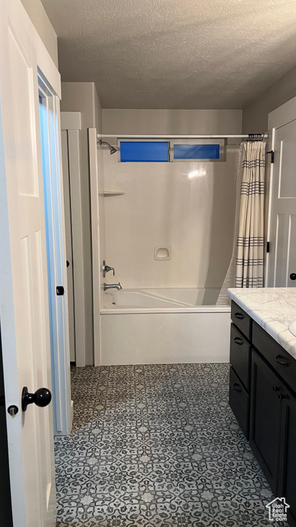 Bathroom with a textured ceiling, shower / bath combo with shower curtain, and vanity