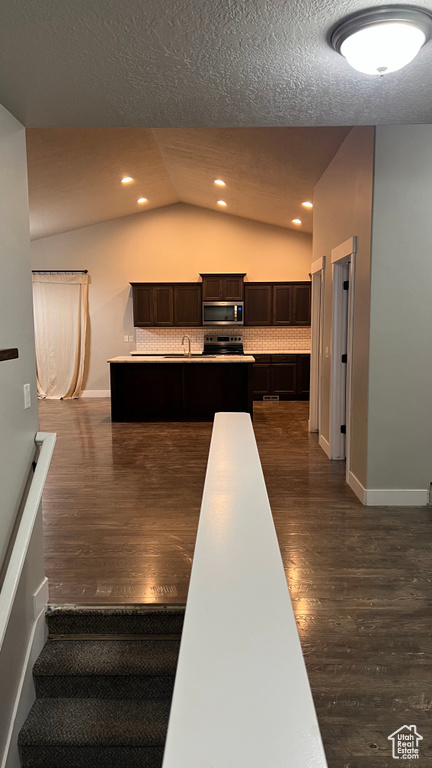 Kitchen with stainless steel microwave, vaulted ceiling, dark wood finished floors, dark brown cabinets, and a textured ceiling