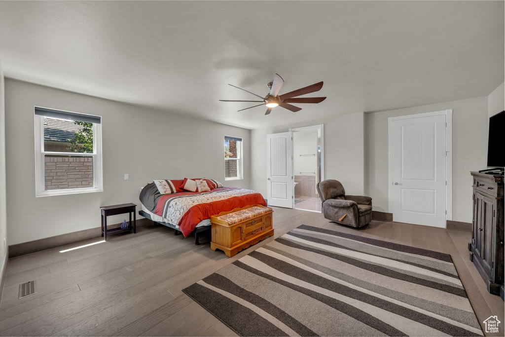 Bedroom with wood finished floors, multiple windows, ensuite bathroom, and ceiling fan