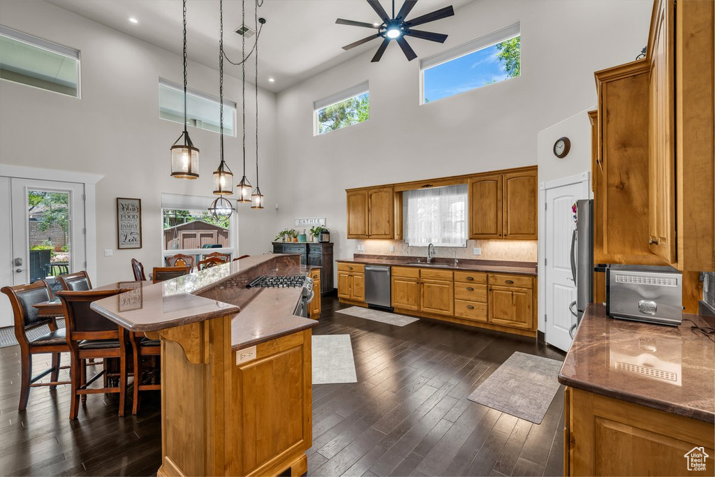Kitchen with stainless steel dishwasher, a high ceiling, ceiling fan, brown cabinetry, and dark wood finished floors