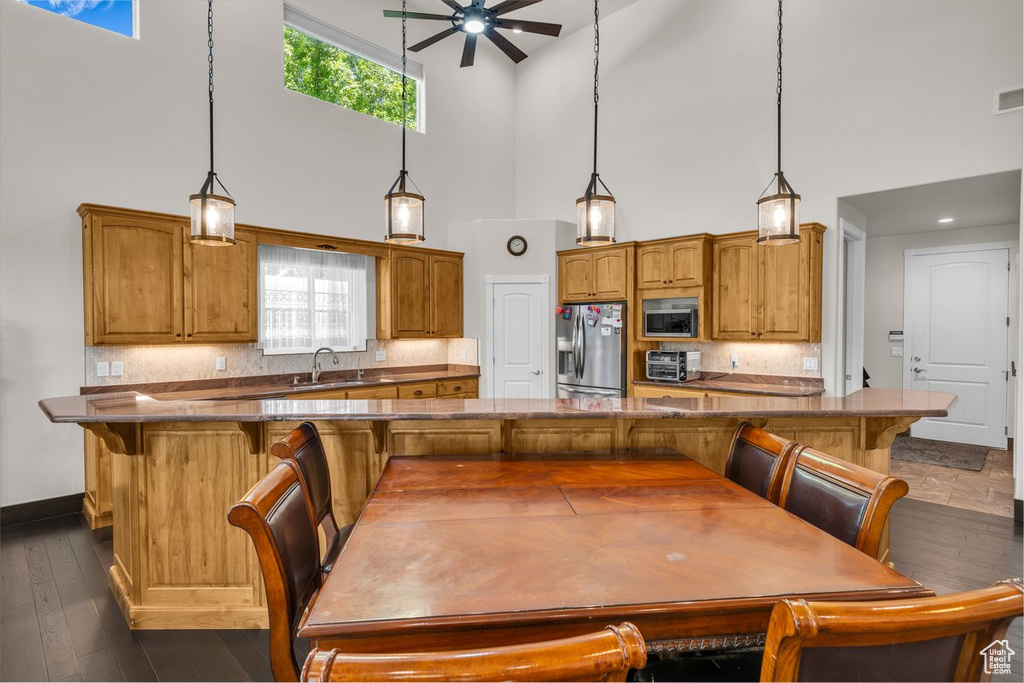 Kitchen featuring stainless steel appliances, a high ceiling, ceiling fan, brown cabinetry, and a breakfast bar area