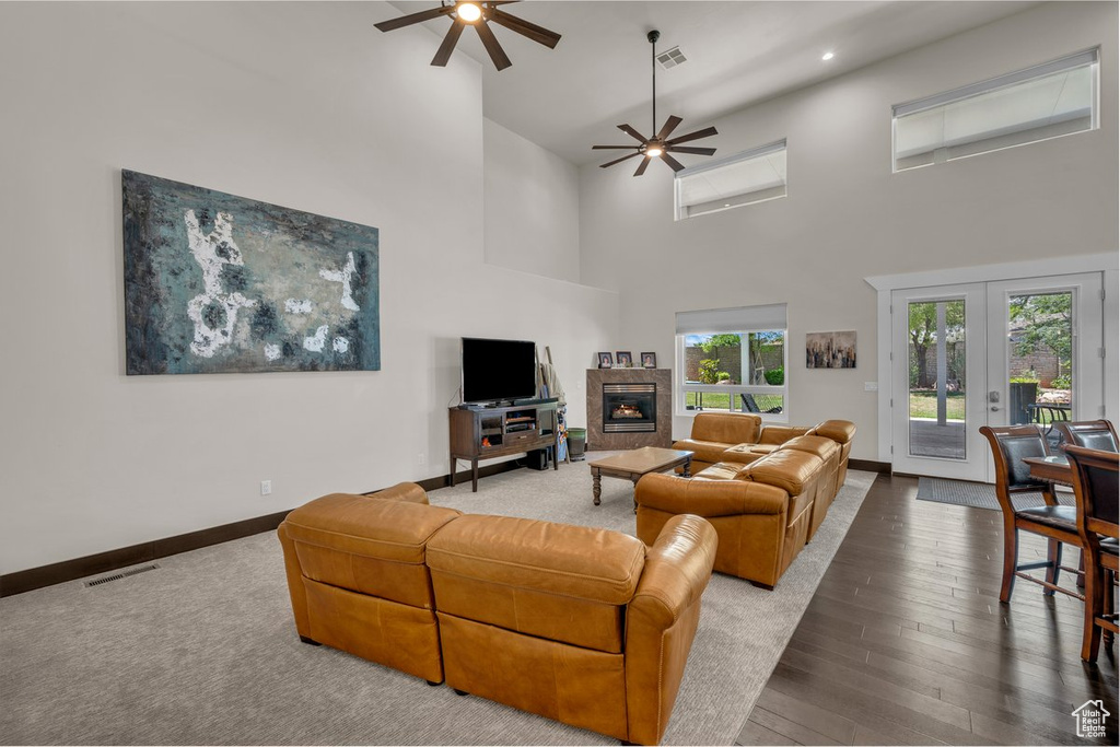 Living room with a ceiling fan, a towering ceiling, a fireplace, wood-type flooring, and recessed lighting