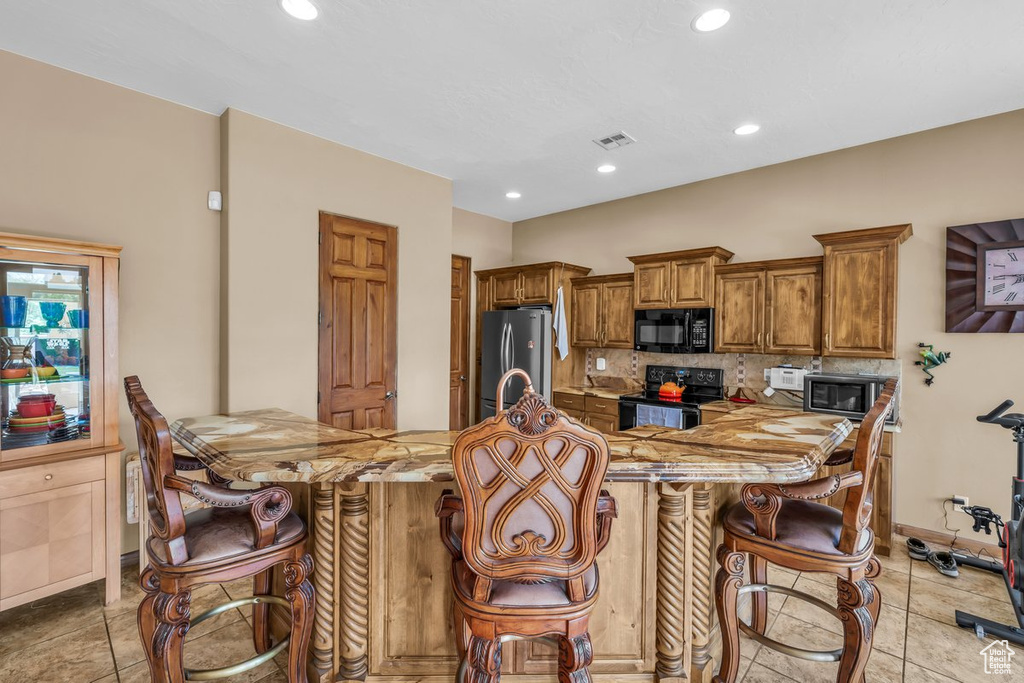 Kitchen with black appliances, a peninsula, brown cabinets, tasteful backsplash, and recessed lighting
