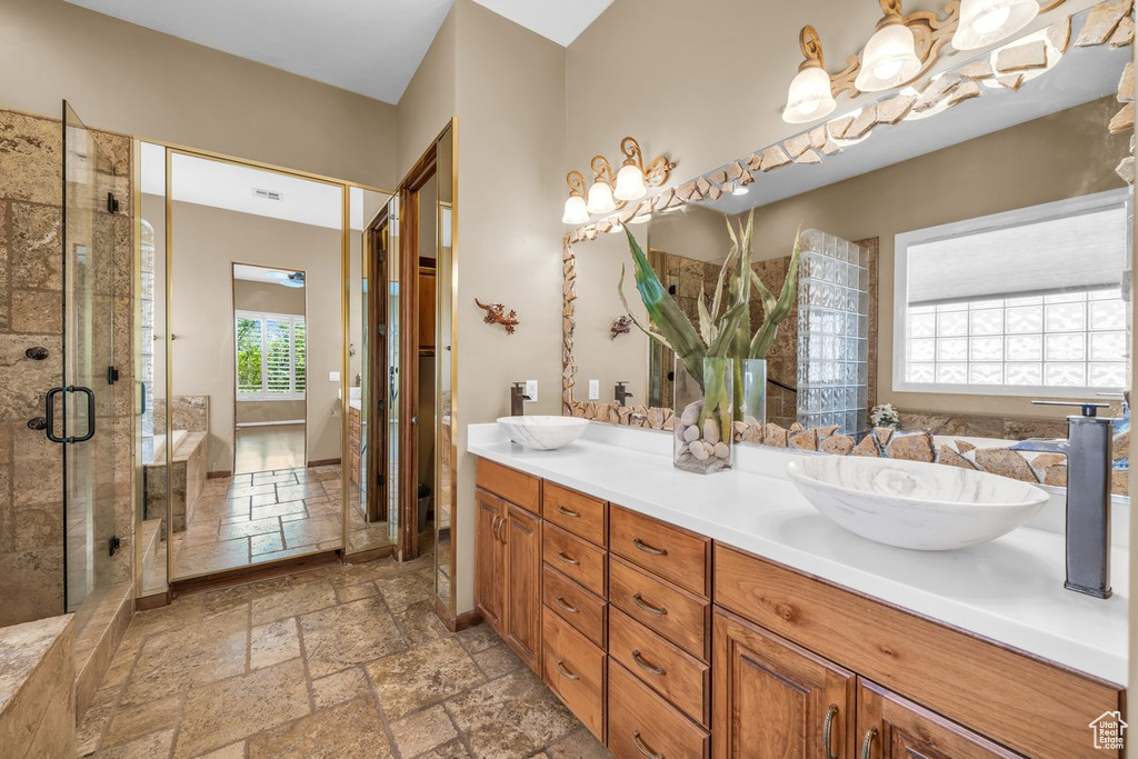 Bathroom featuring stone tile flooring, double vanity, and a shower stall