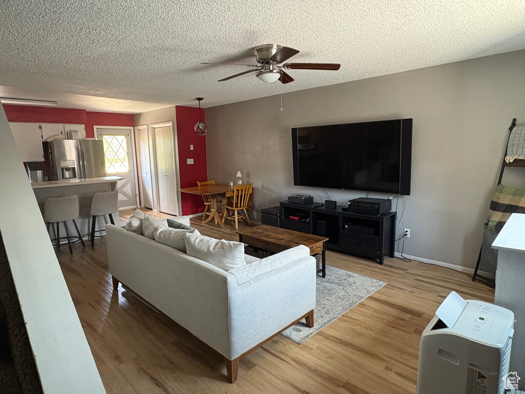 Living area with a ceiling fan, light wood-type flooring, and a textured ceiling