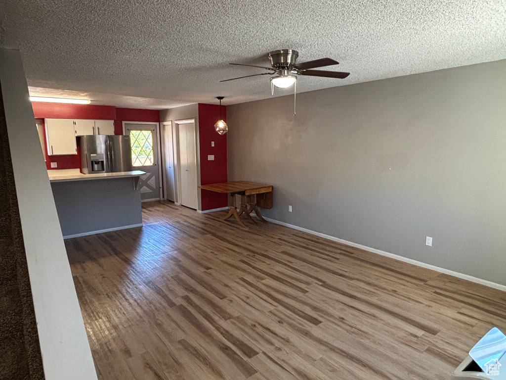 Unfurnished living room with wood finished floors, a ceiling fan, and a textured ceiling