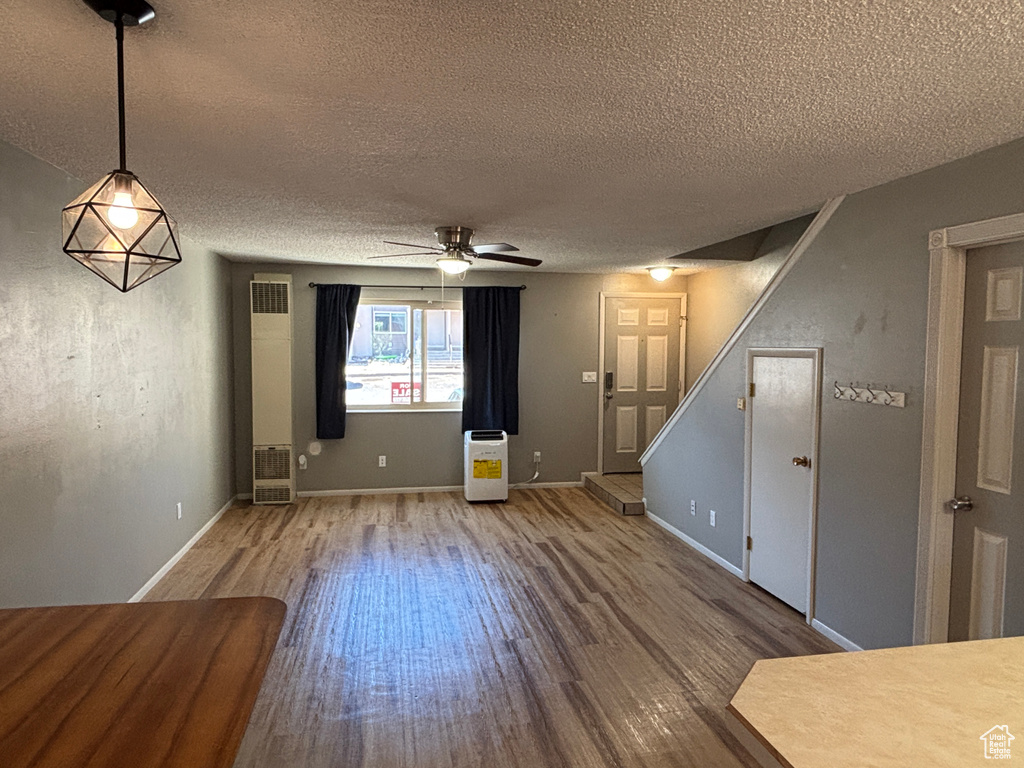 Unfurnished living room with wood finished floors, a textured ceiling, a ceiling fan, and stairway