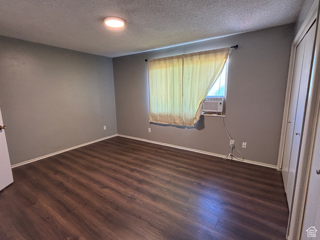 Unfurnished bedroom featuring dark wood-style flooring, a textured ceiling, cooling unit, and a closet