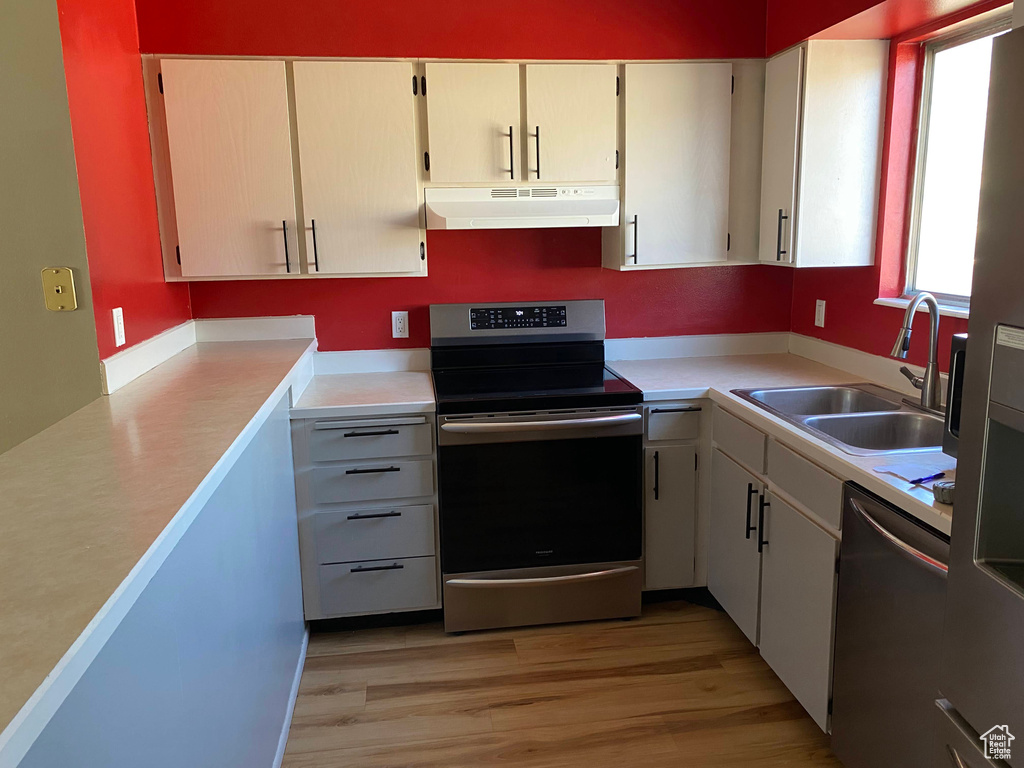 Kitchen with appliances with stainless steel finishes, under cabinet range hood, light countertops, and light wood-style flooring