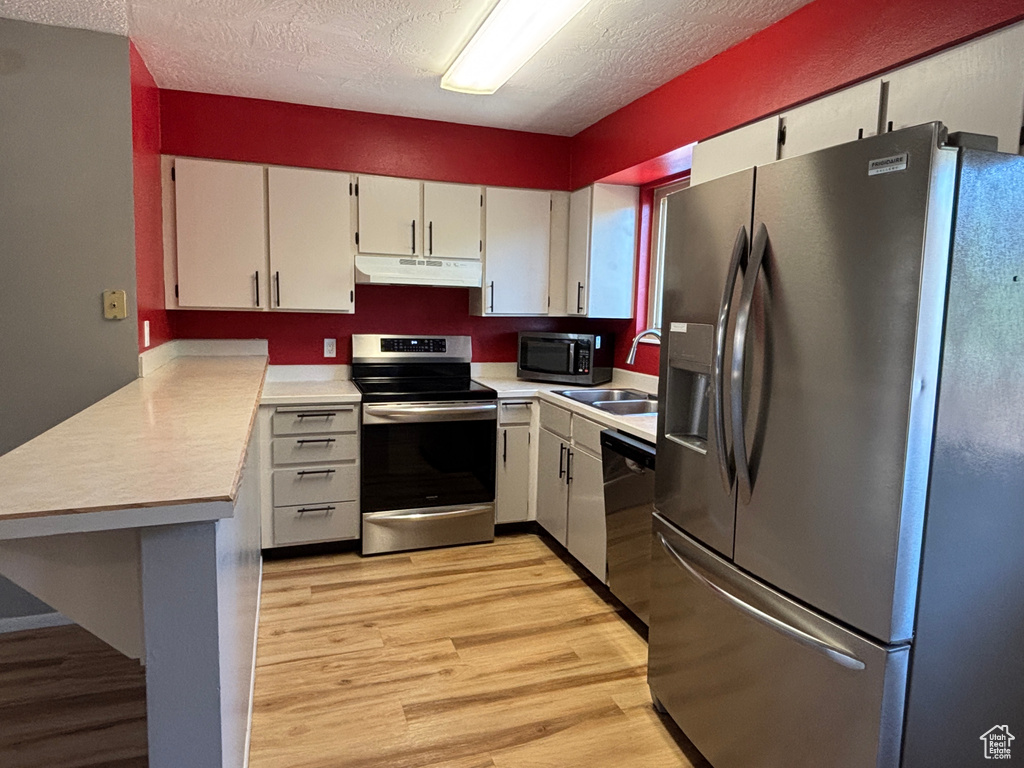 Kitchen with appliances with stainless steel finishes, under cabinet range hood, light countertops, light wood-style floors, and a textured ceiling