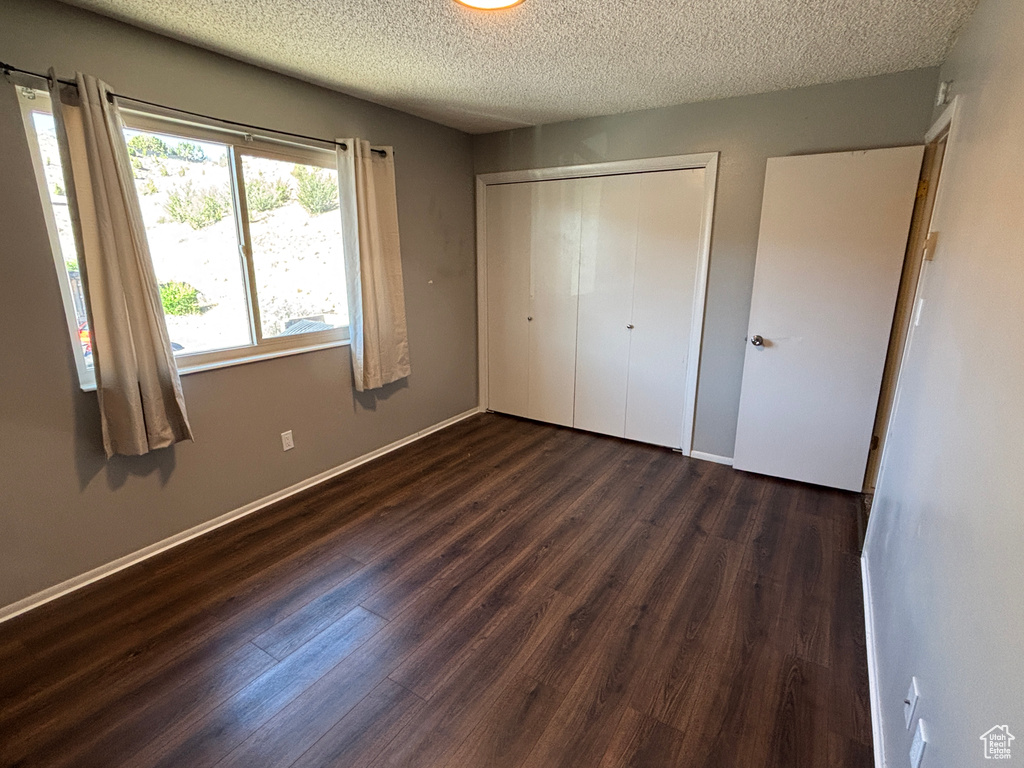 Unfurnished bedroom with a textured ceiling, dark wood-style floors, and a closet