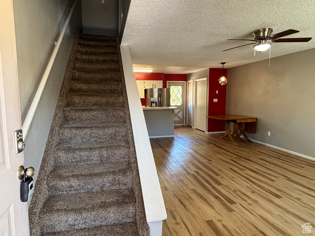 Stairs with wood finished floors, a ceiling fan, and a textured ceiling