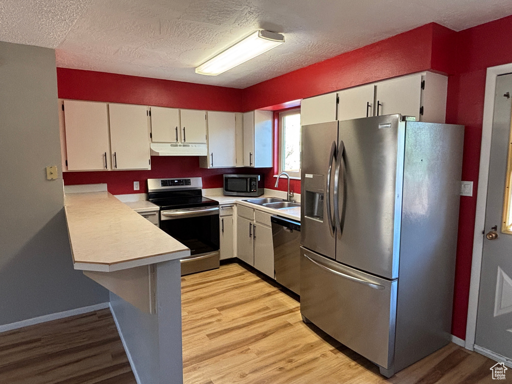 Kitchen featuring appliances with stainless steel finishes, under cabinet range hood, light countertops, a textured ceiling, and light wood finished floors