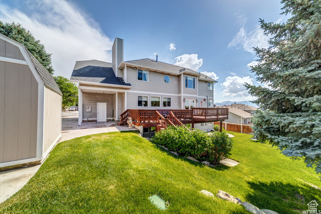 Rear view of property with a chimney, a lawn, a wooden deck, a patio, and roof with shingles
