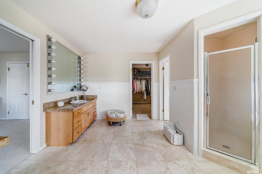Full bath featuring vanity, a shower stall, a wainscoted wall, and a spacious closet