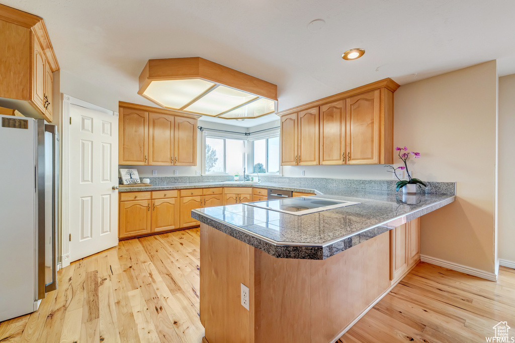 Kitchen with tile countertops, a peninsula, light wood-style flooring, freestanding refrigerator, and electric cooktop