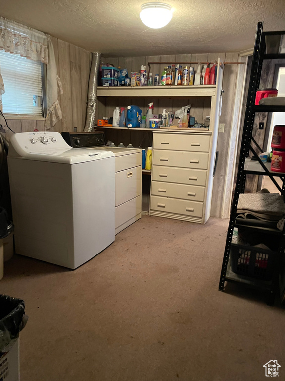 Laundry area with washing machine and clothes dryer, a textured ceiling, wood walls, and light carpet