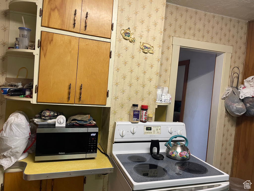 Kitchen featuring white electric stove, wallpapered walls, stainless steel microwave, and light countertops