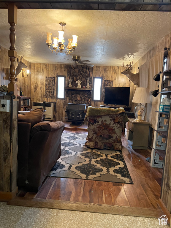 Living area with a wood stove, wood walls, a chandelier, wood finished floors, and a textured ceiling