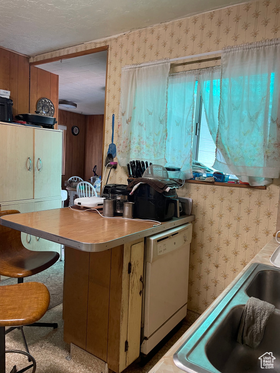 Kitchen featuring white dishwasher, wallpapered walls, light countertops, and a textured ceiling