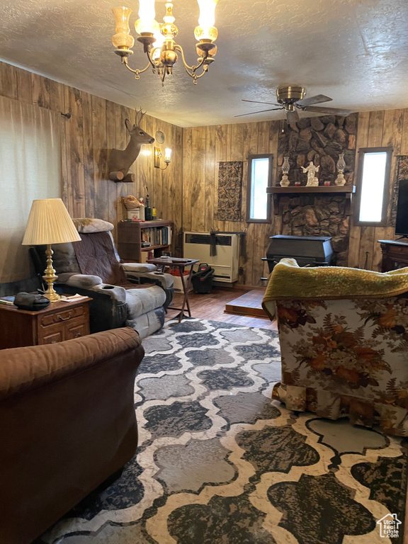 Living area featuring a textured ceiling, wood walls, ceiling fan, a chandelier, and wood finished floors