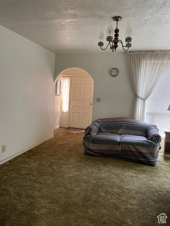 Carpeted living area featuring arched walkways, a chandelier, and a textured ceiling