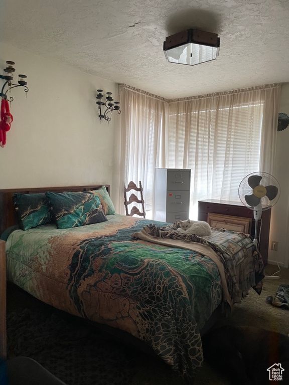 Bedroom with a textured ceiling, multiple windows, and carpet