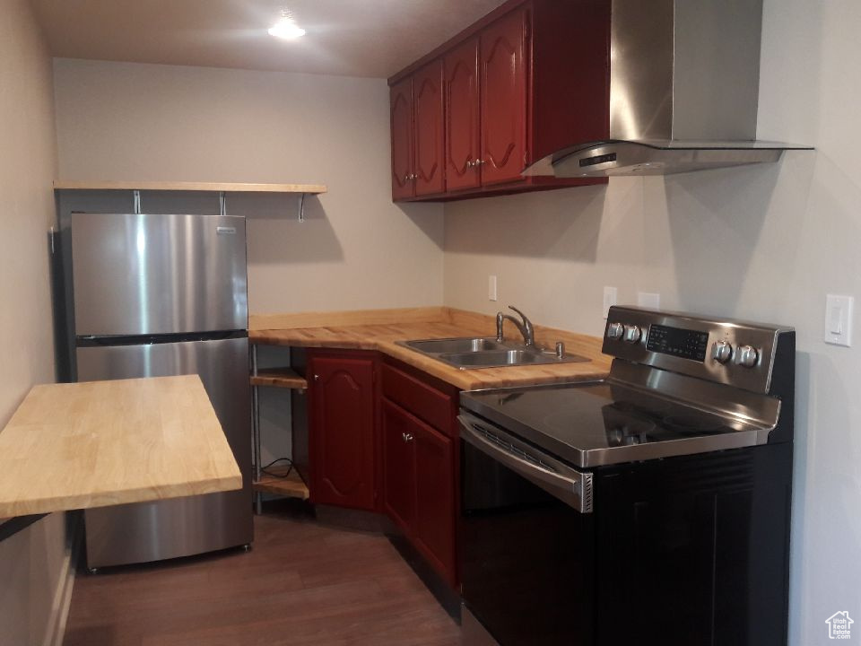 Kitchen featuring wall chimney exhaust hood, freestanding refrigerator, electric stove, wood finished floors, and dark brown cabinets