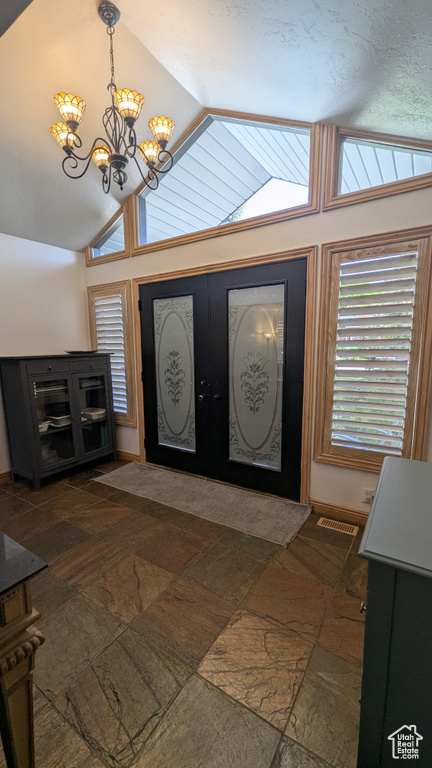 Entryway featuring lofted ceiling, stone tile floors, a chandelier, and french doors