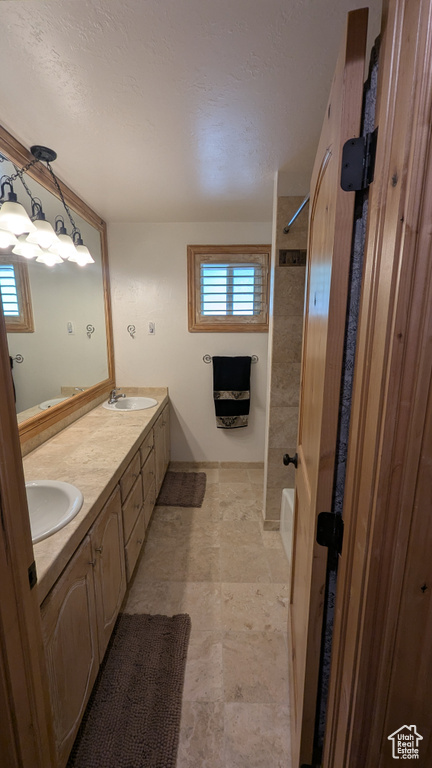 Full bathroom with double vanity, healthy amount of natural light, stone finish flooring, and a textured ceiling