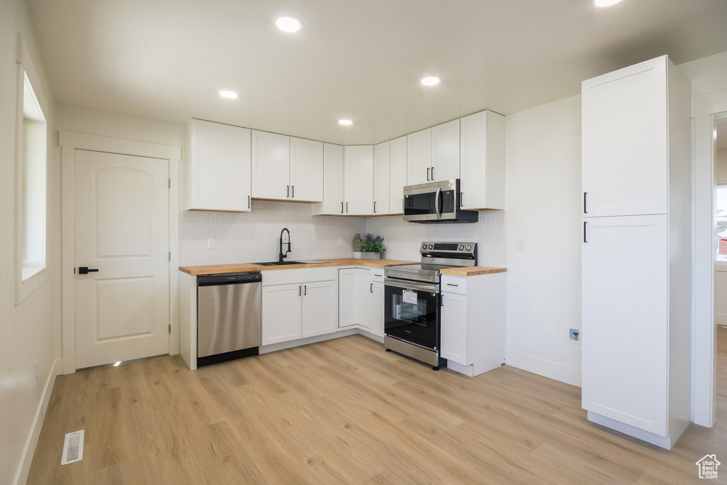Kitchen featuring stainless steel appliances, wood counters, light wood-style flooring, tasteful backsplash, and white cabinetry