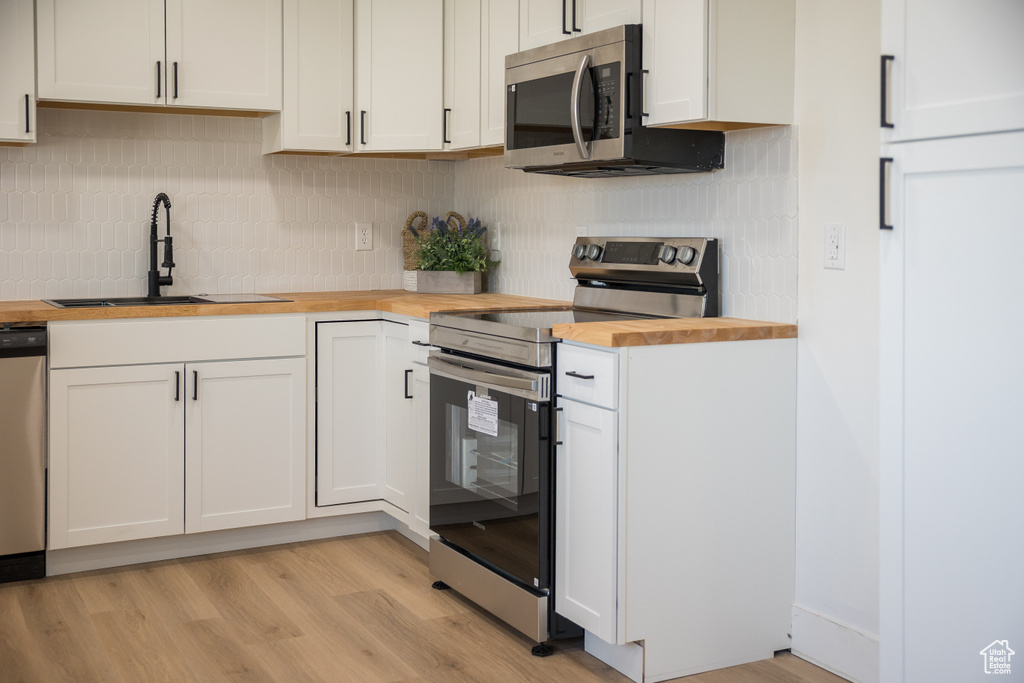 Kitchen featuring wooden counters, appliances with stainless steel finishes, decorative backsplash, light wood-style flooring, and white cabinets