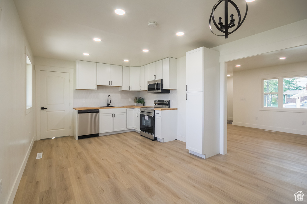 Kitchen featuring stainless steel appliances, light wood-style flooring, recessed lighting, white cabinetry, and wooden counters