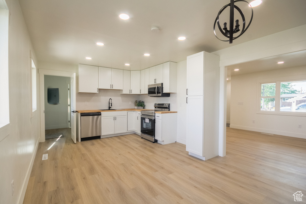 Kitchen featuring stainless steel appliances, a chandelier, light wood finished floors, recessed lighting, and white cabinetry