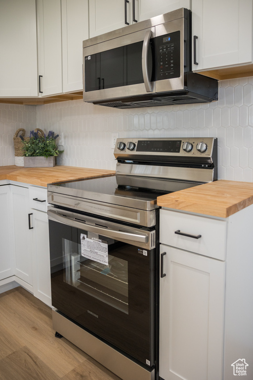 Kitchen featuring stainless steel appliances, butcher block counters, decorative backsplash, and light wood-style flooring