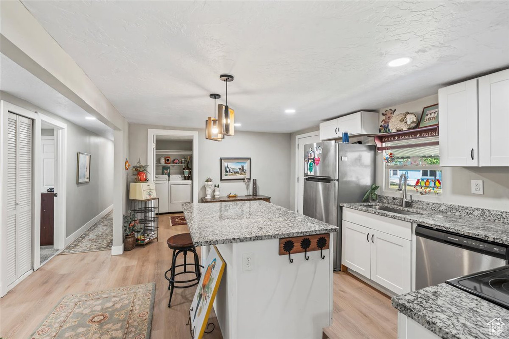 Kitchen with stainless steel appliances, separate washer and dryer, a kitchen island, light wood finished floors, and white cabinetry