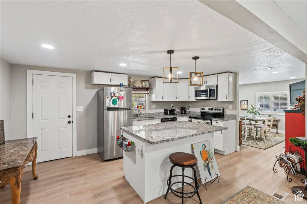 Kitchen with stainless steel appliances, plenty of natural light, a center island, white cabinetry, and recessed lighting