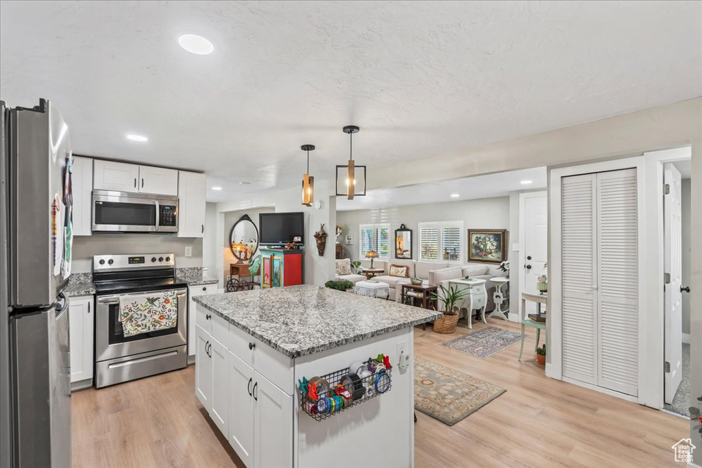 Kitchen with stainless steel appliances, open floor plan, white cabinetry, light stone countertops, and recessed lighting